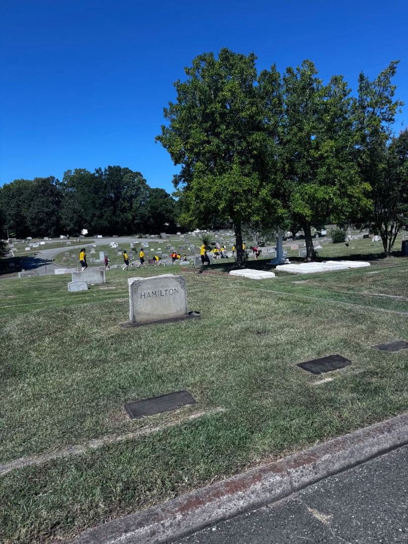 Rows of headstones at Greenwood Cemetery with student volunteers working among them in the distance.